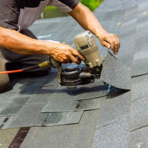 Worker installing shingles on a roof using a nail gun, demonstrating emergency roofing repair services.